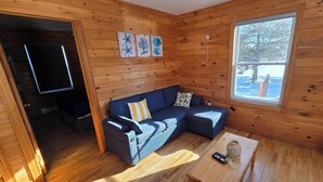 Ein gemütliches Blockhaus-Interieur mit einer Eckcouch, einem kleinen Holztisch und einem Fenster mit Blick auf Bäume.