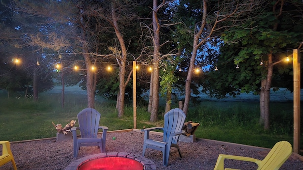 Ein Feuerkorb, umgeben von Adirondack-Stühlen, mit Lichterketten darüber.