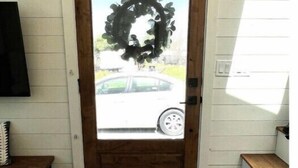 A wooden door with a frosted glass panel, a wreath, and a view of a car outside. - Urban Tiny Home Getaway
 (Caldwell)