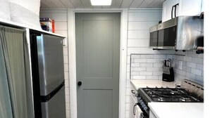 A compact kitchen with a refrigerator, microwave, stove, and white cabinets. - Urban Tiny Home Getaway
 (Caldwell)