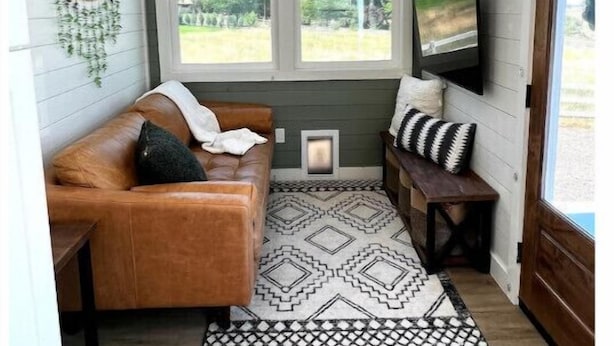 A cozy interior with a leather sofa, a patterned rug, and a television on a wall. - Urban Tiny Home Getaway
 (Caldwell)