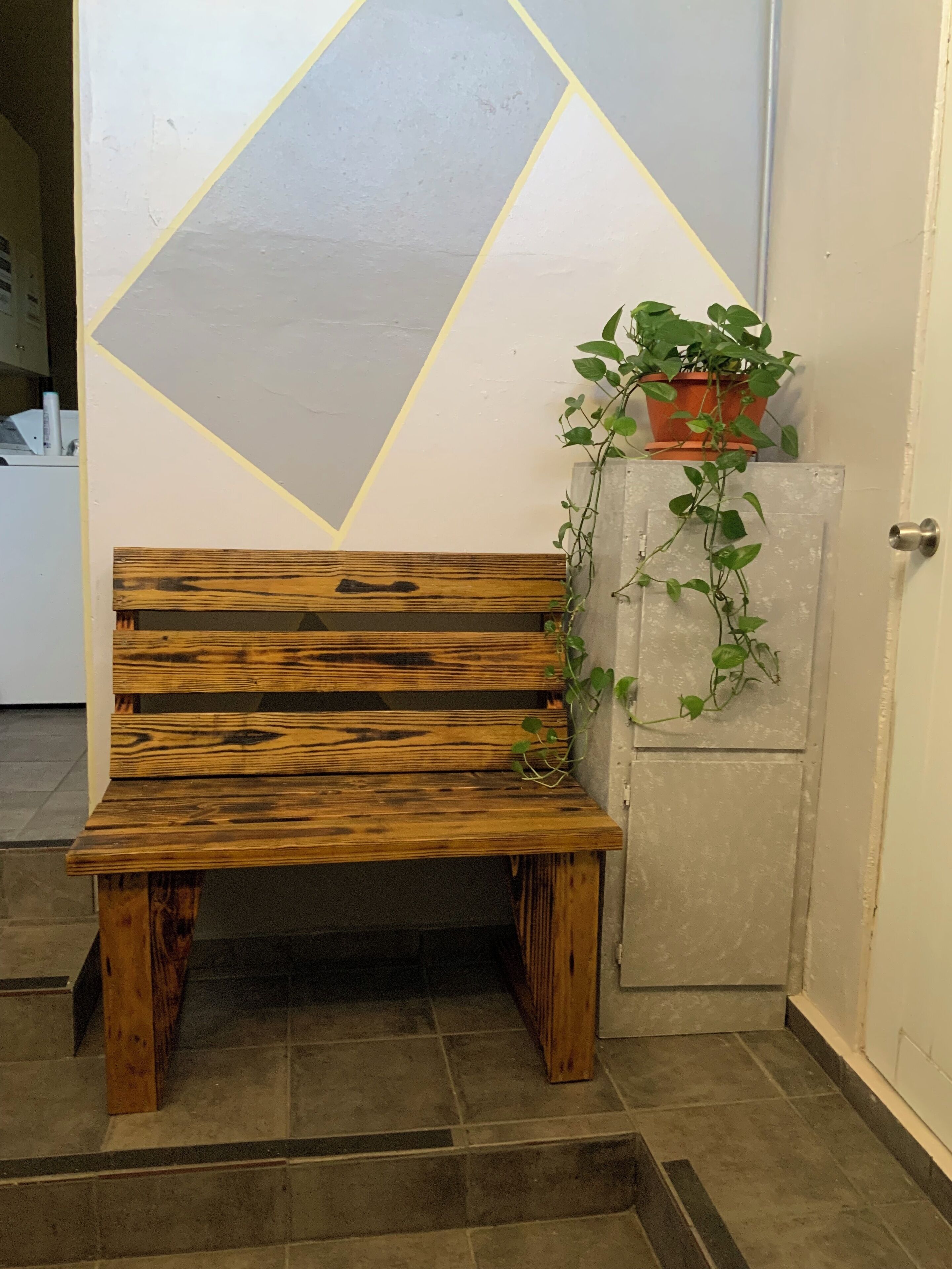 A wooden bench with a potted plant beside it.