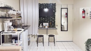 Ett kompakt kök med en kaffemaskin, ett litet matbord och en TV som är monterad på väggen.