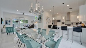 A modern kitchen with white cabinets, a central island, and a dining area with glass-top tables and teal chairs. - Modern & Fun Beach location! Pool, Gym, Spa, Bars & Restaurants to Entertain! (Pompano Beach)