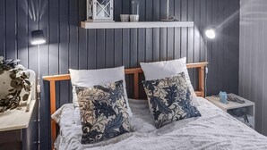 Un lit avec deux coussins décoratifs, une lampe de chevet, une table de chevet avec une lampe et une étagère avec des objets décoratifs.