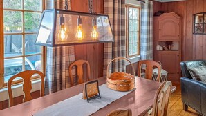 Un coin repas en bois avec une table dressée pour quatre personnes, un luminaire suspendu et une vue sur l’extérieur grâce à de grandes fenêtres.