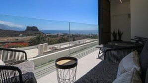 Ein Balkon mit Blick auf das Meer und die Berge, ausgestattet mit einer Couch, Stühlen und einem kleinen Tisch.