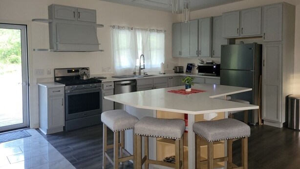 Una cocina moderna con una isla central, taburetes de bar, electrodomésticos de acero inoxidable y armarios de tonos claros.