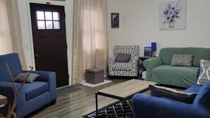 Una sala de estar con un sofá azul, un sofá verde, un sillón estampado, una mesa de centro y un jarrón decorativo.