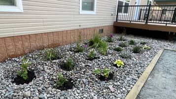 A residential property with a landscaped garden bed, a wooden deck, and a house with siding and windows.