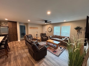 A spacious living room with a fireplace, leather sofas, a coffee table, and a dining area with a kitchen in the background.