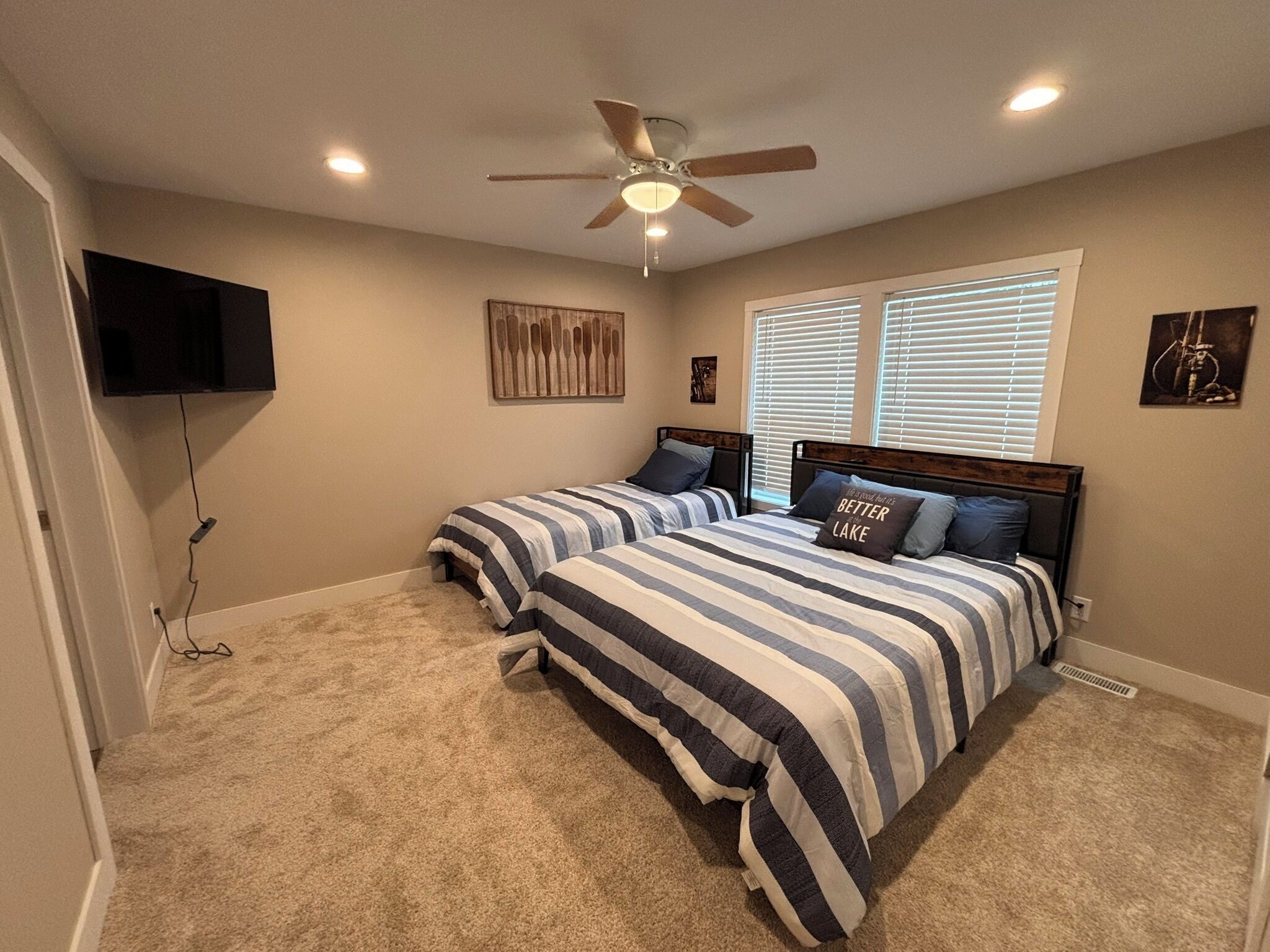A bedroom with two beds, a ceiling fan, a TV mounted on the wall, and artwork.