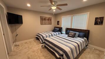 A bedroom with two beds, a ceiling fan, a TV mounted on the wall, and artwork.