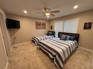A bedroom with two beds, a ceiling fan, a TV mounted on the wall, and artwork. - New 4BR/2BA Lake of the Woods Walleye Camp! (Baudette)