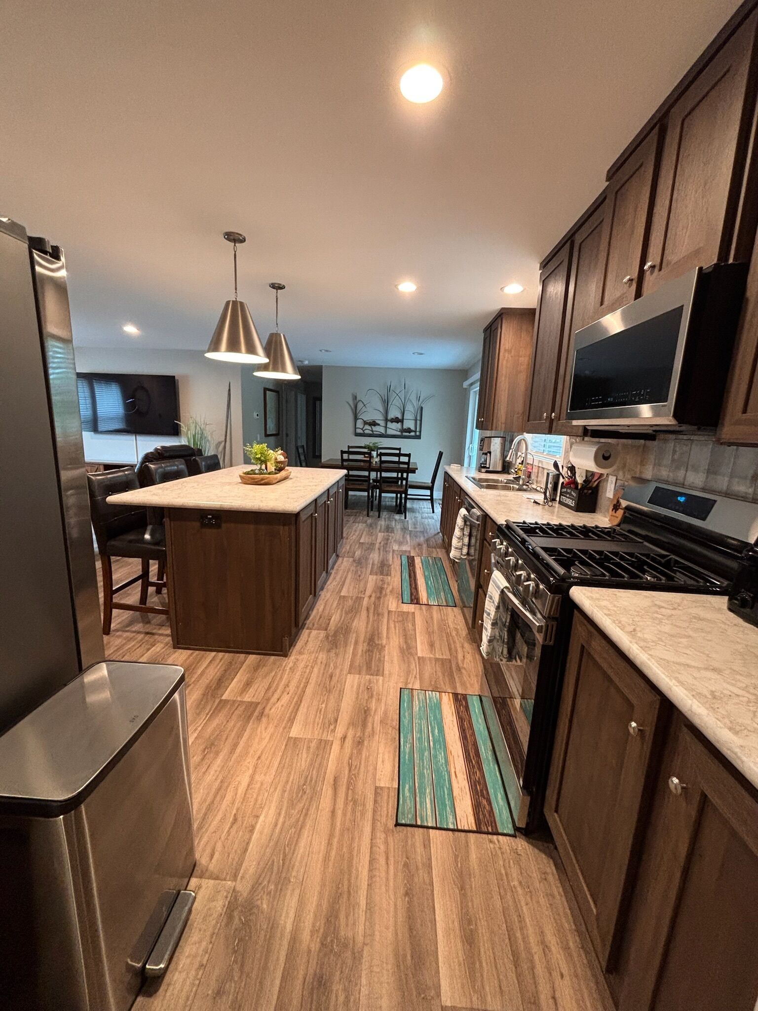 A modern kitchen with wooden cabinets, a central island, stainless steel appliances, and pendant lighting.