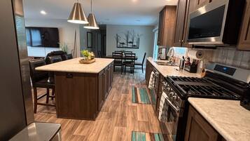 A modern kitchen with wooden cabinets, a central island, stainless steel appliances, and pendant lighting.