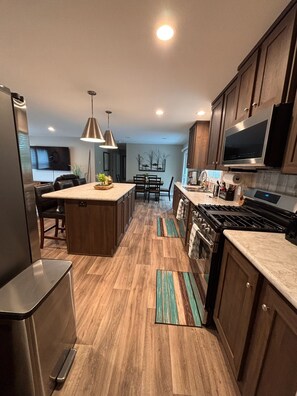 A modern kitchen with wooden cabinets, a central island, stainless steel appliances, and pendant lighting. - New 4BR/2BA Lake of the Woods Walleye Camp! (Baudette)