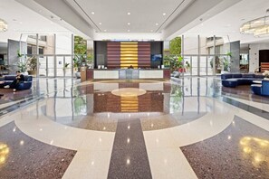 A spacious lobby with a central reception desk, seating areas, and a polished floor. - ModernBohoOasis | 2BR 2BA | Gym&Pool | Mins to DC (Arlington)