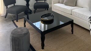 A modern living room with a white sofa, two black chairs, a glass coffee table, and a chandelier.