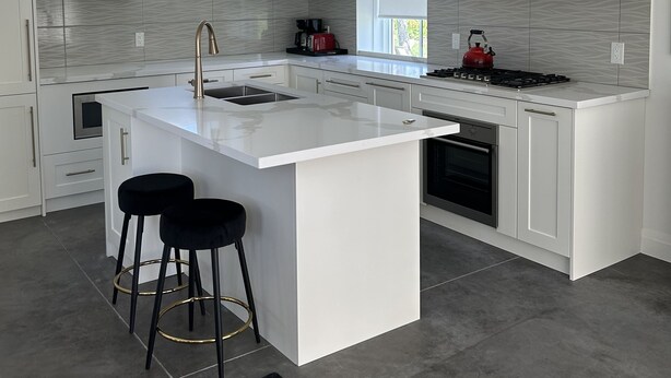 A modern kitchen with white cabinetry, a central island with stools, a black range hood, and a built-in oven.