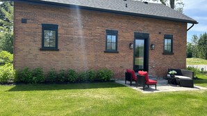 A brick building with a flat roof, a front door, and two windows. There is a small patio area with outdoor furniture.