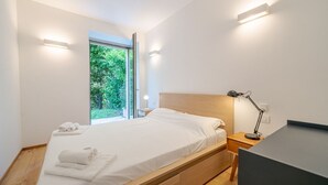 Een moderne slaapkamer met een bed, nachtkastjes en een raam met uitzicht op groen.
