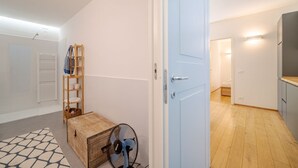 Een kamer met een houten vloer, een witte deur, een ventilator, een klein houten tafeltje en een plank met spullen.