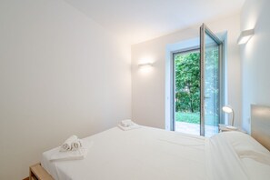 A bedroom with a large bed, a glass door leading to a balcony, and a bedside table with a lamp.