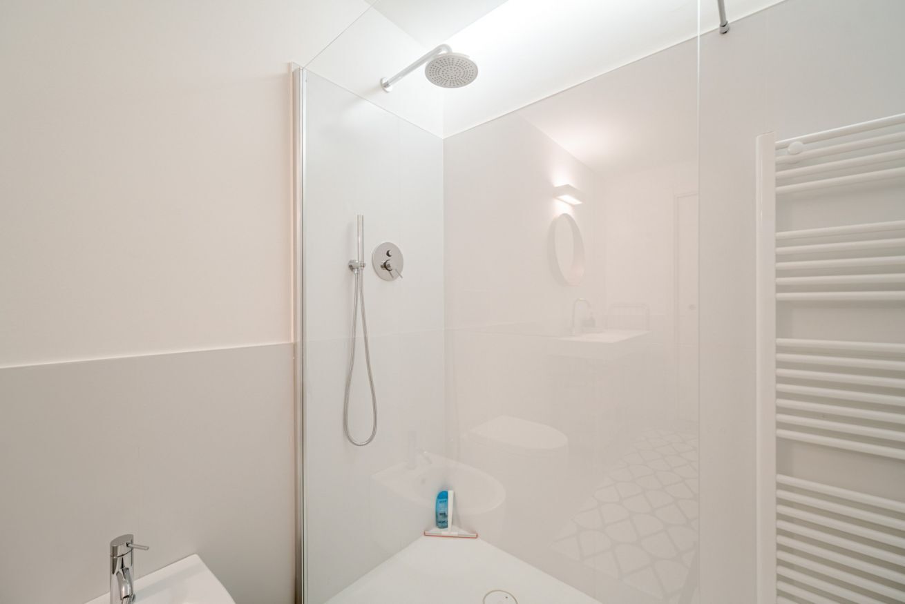 A modern shower area with a glass door, a handheld showerhead, and a wall-mounted control panel.