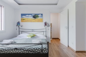 A bedroom with a bed, a painting, a bookshelf, and a door.