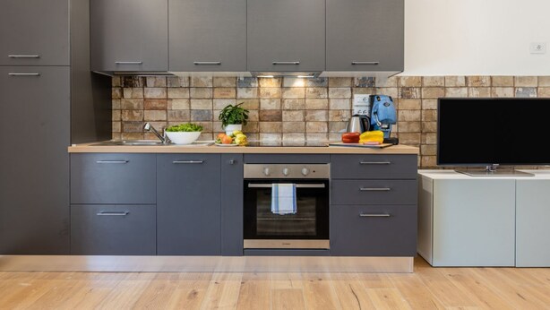 Een moderne keuken met grijze kastjes, een betegelde spatwand, een inbouwoven en een flatscreen televisie.