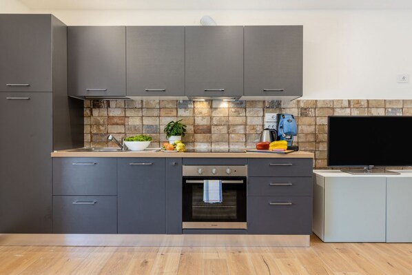 A modern kitchen with grey cabinets, a tiled backsplash, a built-in oven, and a flat-screen TV.