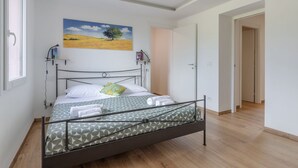 Een slaapkamer met een bed, een schilderij, een boekenplank en een deur.