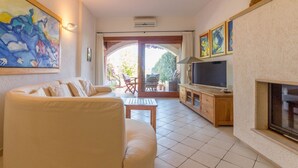 Een woonkamer met een bank, televisie, open haard en uitzicht door een glazen deur op een buitenruimte.
