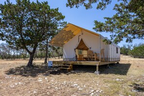 A single-story, A-frame-style tent with a wooden deck and seating area. - Off-Grid Hill Country Glamping Tent (Boerne)