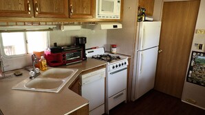 A compact kitchen with wooden cabinets, a microwave, a stove, a sink, and a refrigerator.
