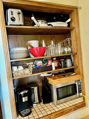 Una cocina con tostadora, microondas y diversos utensilios de cocina en estantes.