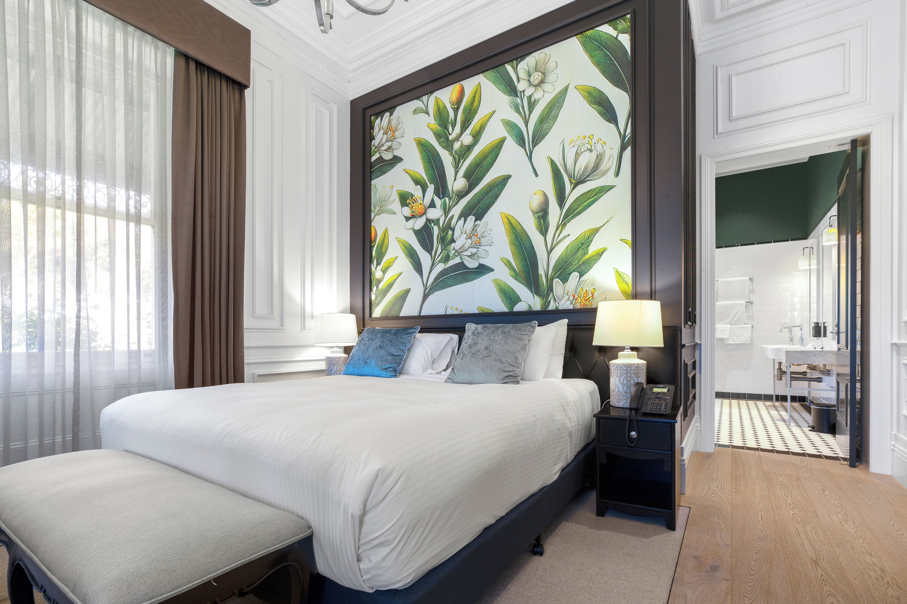 A neatly arranged bedroom with a large bed, bedside tables, a nightstand, and a painting above the bed.