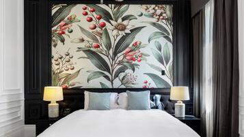 A bedroom with a large bed, a chandelier, a floral wallpaper, and two bedside tables with lamps.