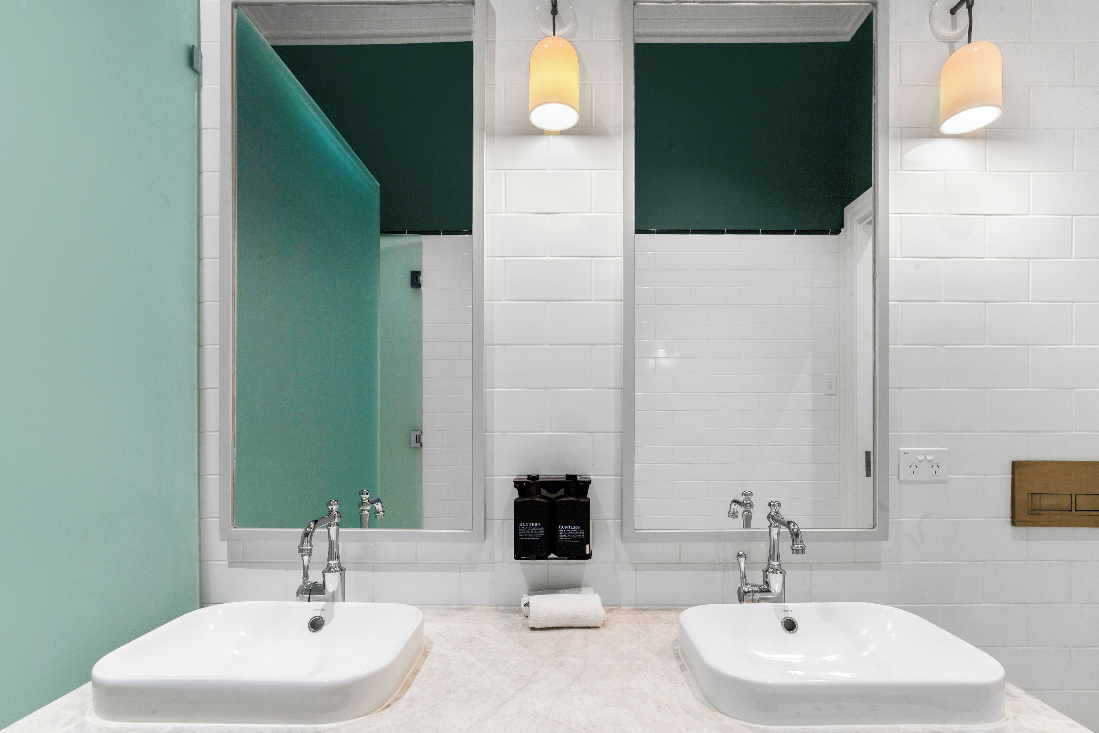 A modern bathroom with two sinks, white tiled walls, and teal accents.