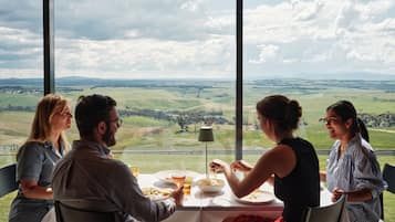 Une table à manger où sont assis quatre convives, donnant sur un paysage magnifique grâce à de grandes fenêtres.