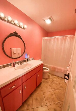 Une salle de bain avec un mur rose, un miroir rond, un lavabo et des toilettes.
