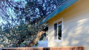 Una terraza de madera con una pequeña mesa y dos sillas, una valla metálica y un edificio con una ventana.
