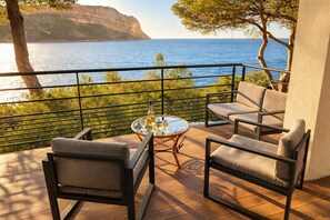 A balcony with a view of the sea, furnished with two chairs and a table with a bottle and glasses.