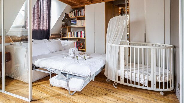 Une chambre avec un lit en mezzanine, un berceau, une bibliothèque et une fenêtre avec des rideaux.