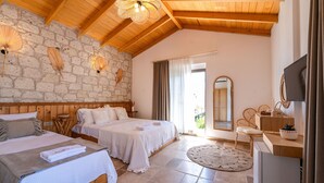 A bedroom with two beds, a stone wall, wooden ceiling beams, a round rug, and a television on a wooden dresser. - Hatica by Fora Alaçatı (Cesme)