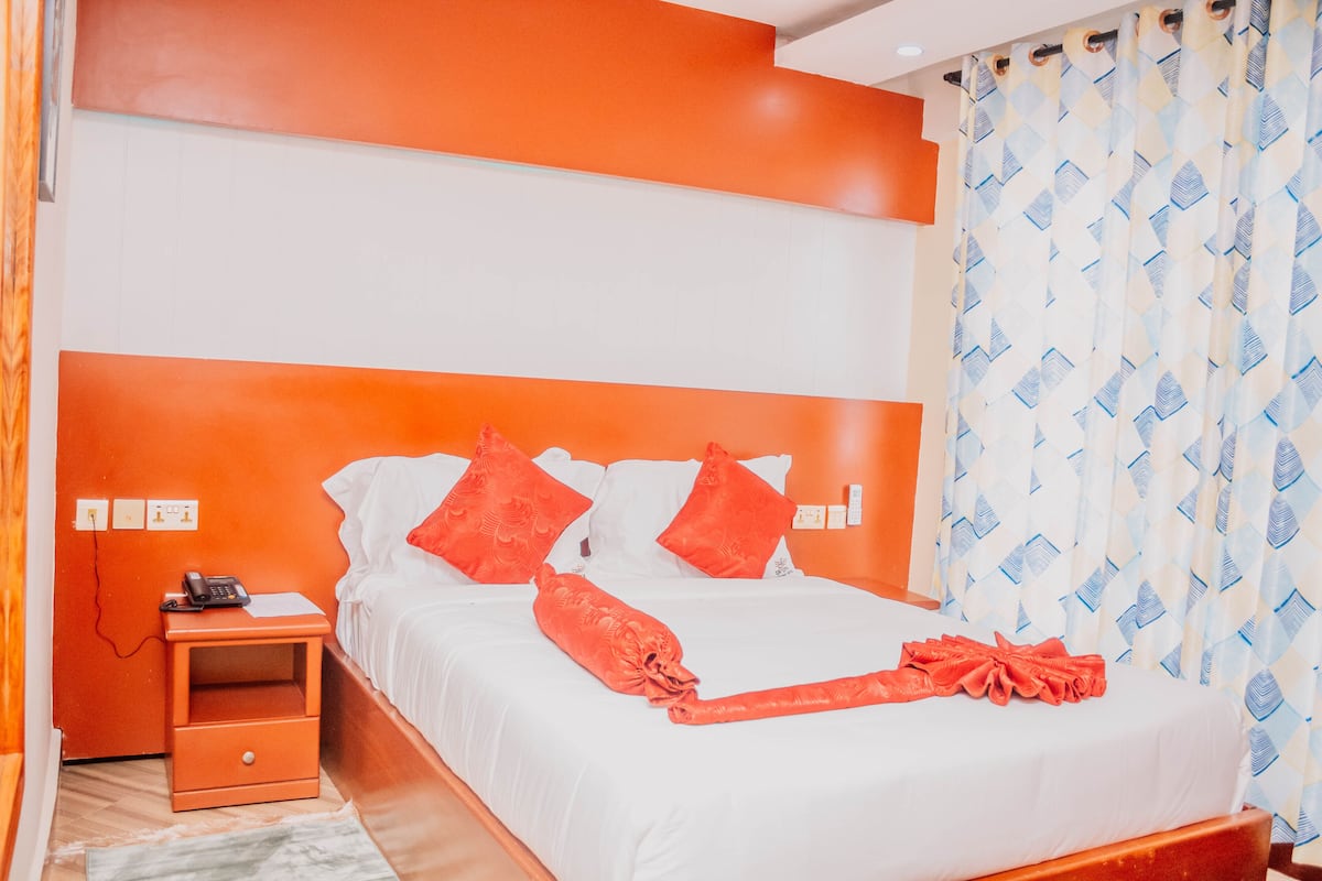 Una habitación de hotel con una cama grande, paredes anaranjadas y una cortina estampada.