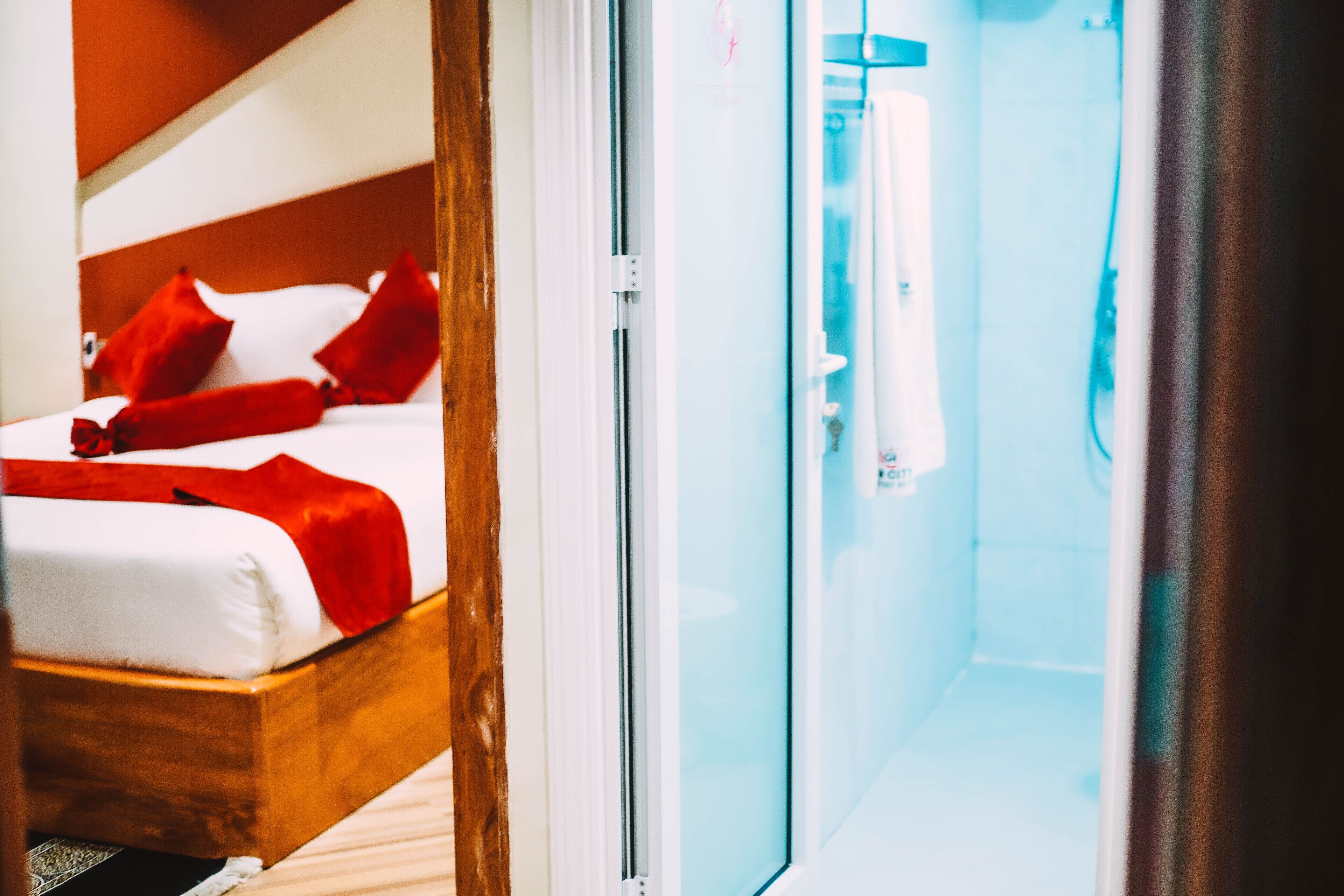 A hotel room with a bed, red pillows, and a glass shower enclosure.
