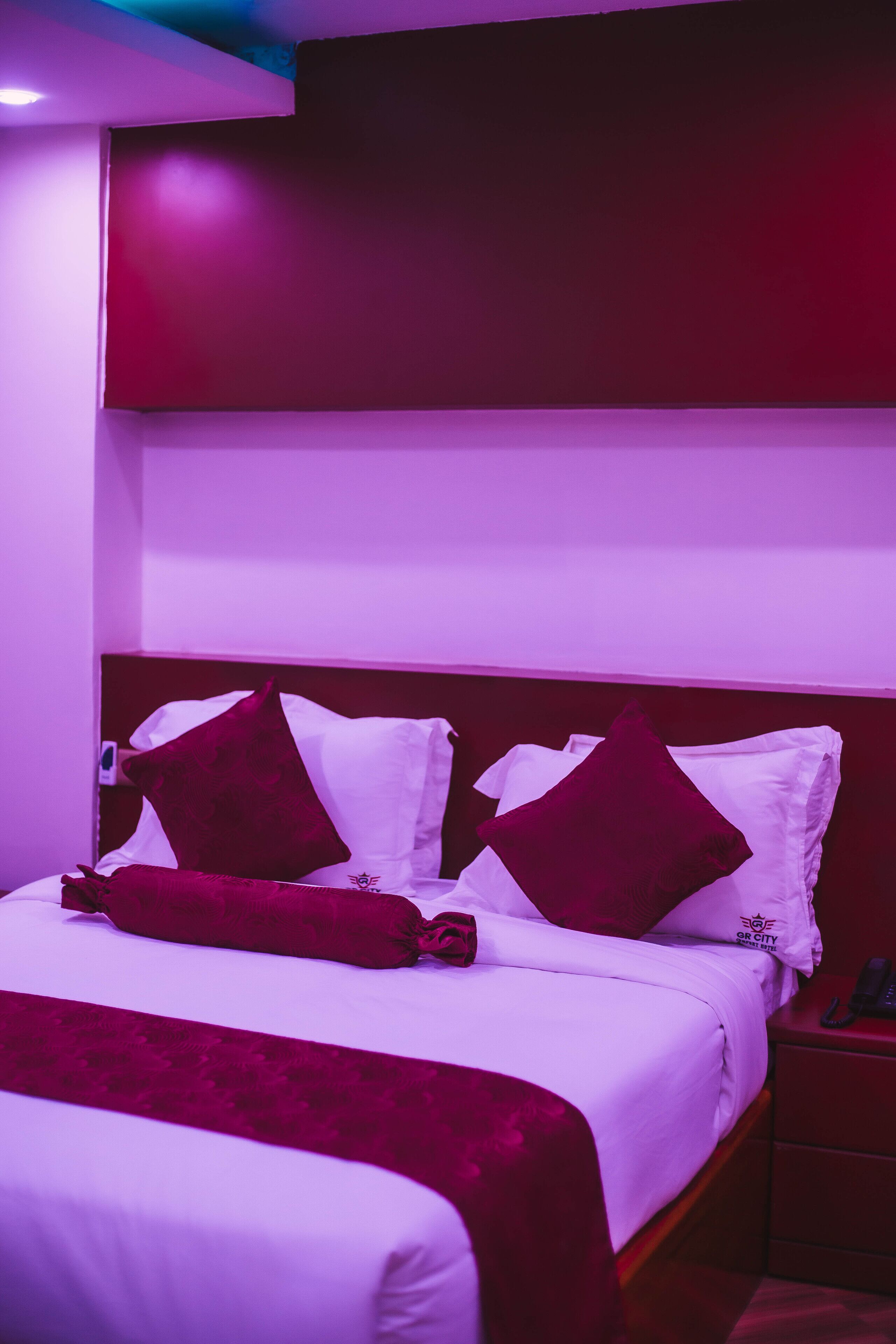 A hotel room with a bed, pillows, a bedside table, and a nightstand.
