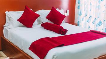 A neatly made bed with white linens and red pillows, a red throw blanket, and a wooden headboard.